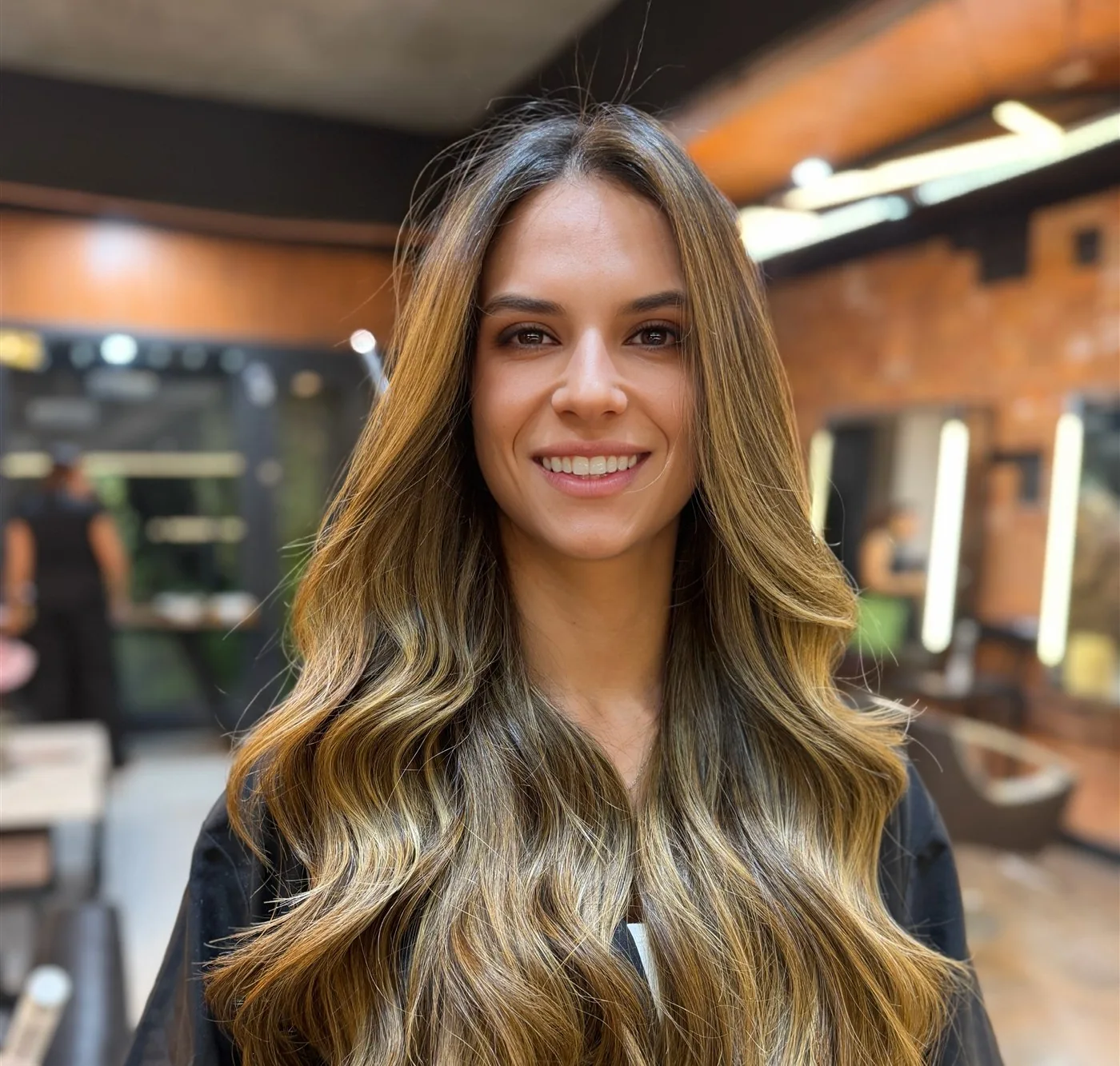 Cliente da HAAR by RUPP sorrindo com balayage iluminado, ondas longas e brilho